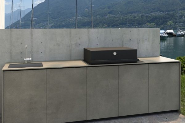 Valsot Outdoor-Küche mit Betonfronten, Spülbecken und Grill, platziert vor einer Hafen- und Bergkulisse.
